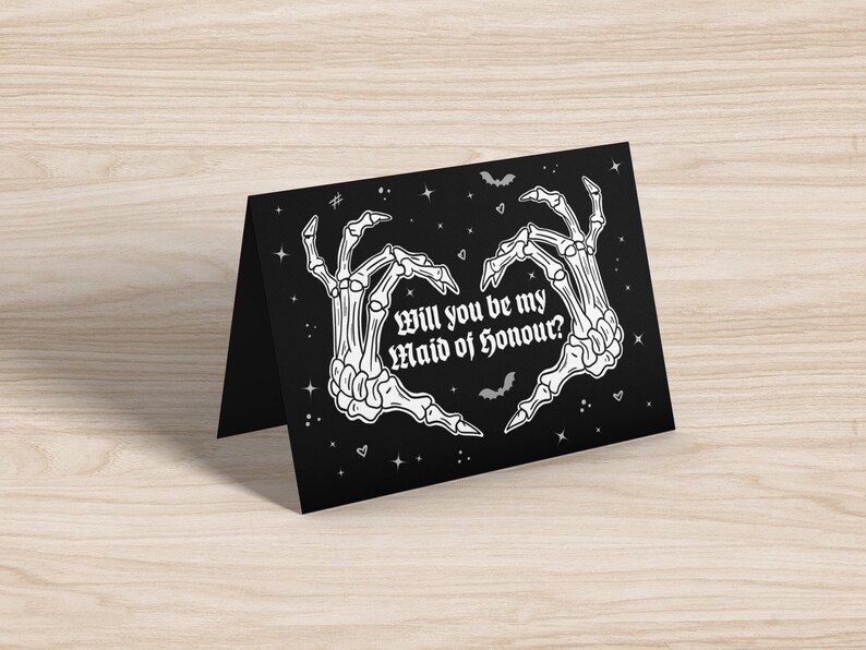 May include: Black card with white skeleton hands forming a heart shape. The text reads "Will you be my Maid of Honour?" with stars and bats in the background.