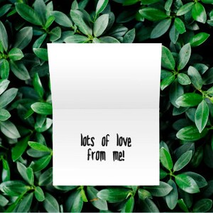 K&ouml;nnte beinhalten: Eine wei&szlig;e Karte mit dem Text "lots of love from me!" in schwarzer Tinte. Die Karte ist von gr&uuml;nen Bl&auml;ttern umgeben.