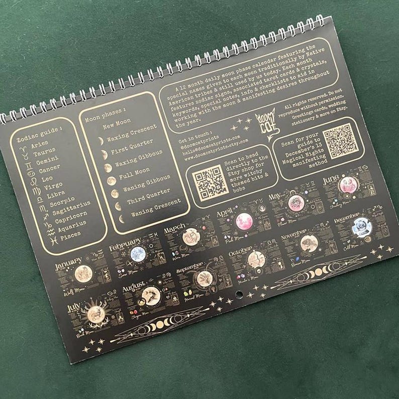 May include: A spiral-bound, black 12-month moon phase calendar. It features zodiac signs, moon phases, and associated tarot cards. The calendar includes text such as "Moon Phases" and "Zodiac Guide". The calendar is designed to aid in working with the moon and manifesting desires.