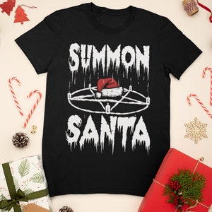 May include: Black t-shirt with the text "SUMMON SANTA" in a dripping font, featuring a pentagram with a Santa hat in the center. The shirt is surrounded by Christmas decorations, including wrapped gifts, candy canes, and pine cones.