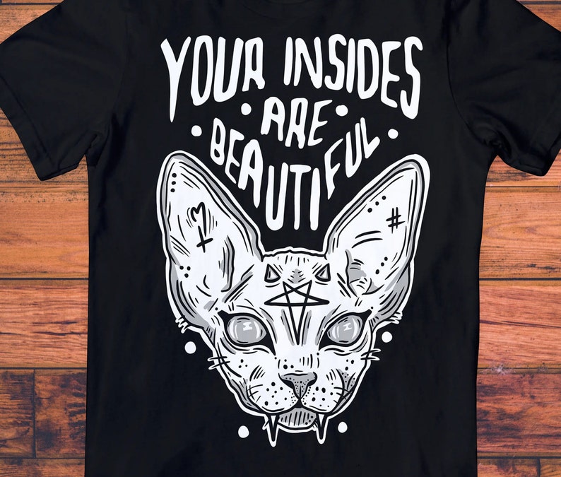 May include: Black t-shirt with a white graphic of a sphinx cat with a pentagram on its forehead. The text "YOUR INSIDES ARE BEAUTIFUL" is above the cat.