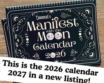 May include: A black spiral-bound wall calendar titled Doomcat's Manifest with the Moon Calendar 2026, featuring white decorative celestial illustrations of moons, stars, and clouds, with the text This is the 2026 calendar 2027 in a new listing!