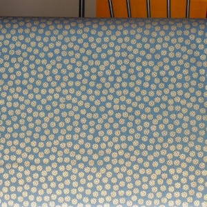 Op de afbeelding: Een blauwe stof met een wit madeliefjespatroon. De stof heeft een subtiele glans en een gladde textuur.