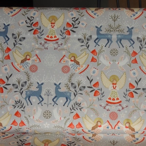 May include: A gray fabric with a repeating pattern of angels, deer, and floral designs. The angels are wearing white dresses with red and blue accents. The deer are blue and white. The floral designs are red, white, and blue.