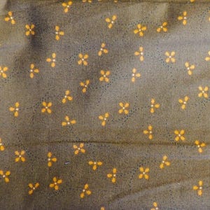 May include: A brown fabric with a repeating pattern of small orange four-petal flowers.