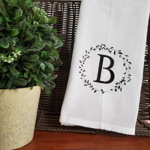 May include: White kitchen towel with a black floral wreath design and the letter "B" in the center.
