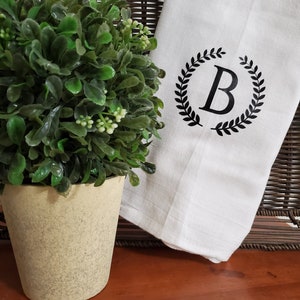 May include: White kitchen towel with a black wreath design and the letter "B" in the center.