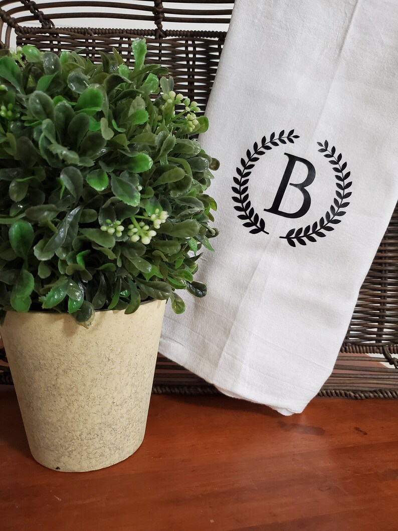 May include: White kitchen towel with a black wreath design and the letter "B" in the center.
