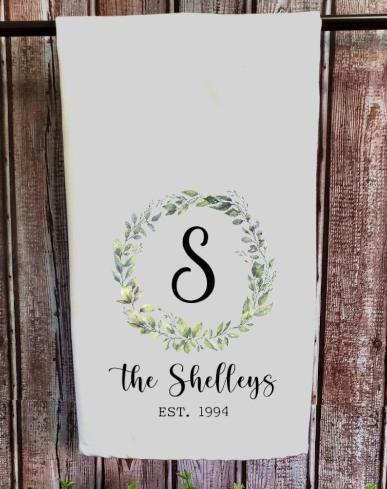 May include: White kitchen towel with a green leafy wreath and the letter "S" in the center. The text "The Shelleys EST. 1994" is printed below the wreath.