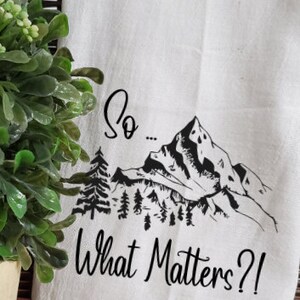 May include: White kitchen towel with a black mountain range design and the text "So... What Matters?!"