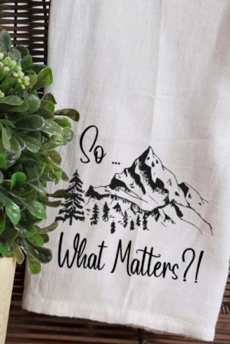 May include: White kitchen towel with a black mountain range design and the text "So... What Matters?!"