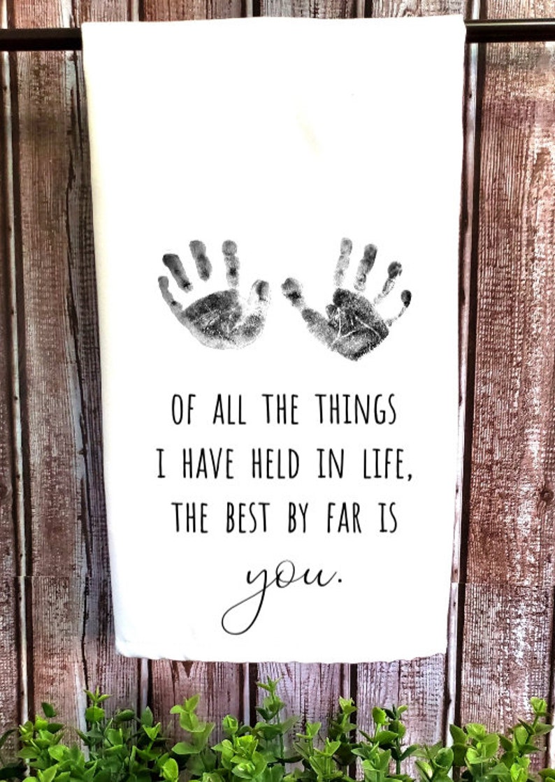 May include: A white kitchen towel with two black handprints and the text "OF ALL THE THINGS I HAVE HELD IN LIFE, THE BEST BY FAR IS you."