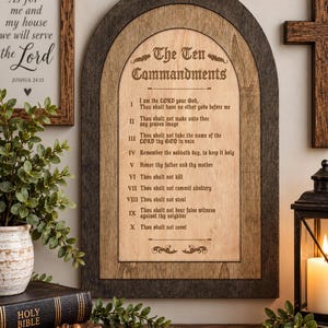 May include: An arched wooden wall plaque featuring the Ten Commandments engraved in black text on a light wood center panel, framed by a dark stained wood border. The text lists the ten commandments from I to X in a traditional font style.