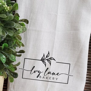 May include: White kitchen towel with a black logo that says "ivy lane bakery" with a simple leaf design.
