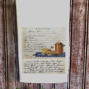 May include: A white tea towel with a vintage recipe card printed on it. The recipe card is for pecan pie and includes a list of ingredients and instructions. The card is illustrated with a pie and a copper pot.