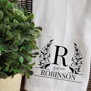 May include: White kitchen towel with a black floral design and the letter "R" in the center. The text "Est. 2021 ROBINSON" is printed below the letter.