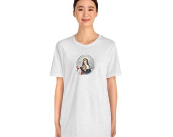 May include: A light gray t-shirt featuring a circular graphic of a religious figure holding flowers, with text. The graphic is in a vintage style. The shirt is a crew neck and has short sleeves.