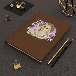 Puede incluir: Un diario marrón con el texto "whoever eats this bread will live forever" y una ilustración de una mujer con un halo. También se ven lápices dorados y negros y clips dorados.