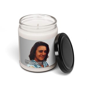 May include: A white candle in a clear glass jar with a black lid. The candle has a label with a portrait of a woman and the text "Bl. Chiara Luce Badano Pray for us!"