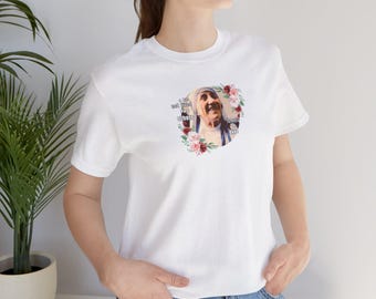 May include: White t-shirt featuring a portrait of a woman surrounded by a floral wreath. The text on the shirt reads "A life not lived for others is not a life." The shirt is made of a soft material.