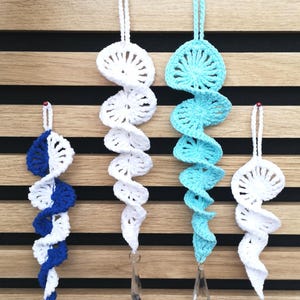 Könnte beinhalten: Vier spiralförmige Häkelornamente mit Aufhängeschlaufen. Eines ist blau-weiß, eines ist einfarbig weiß, eines ist hellblau mit einem klaren Kristallprisma am unteren Ende und eines ist einfarbig weiß. Jedes Stück hat ein strukturiertes, kreisförmiges Muster.