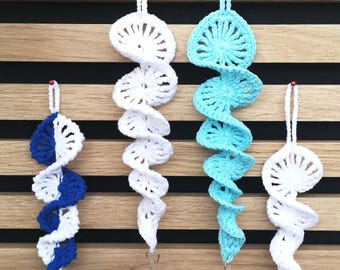 May include: Four spiral crochet ornaments with hanging loops. One is blue and white, one is solid white, one is light blue with a clear crystal prism at the bottom, and one is solid white. Each piece features a textured, repeating circular pattern.