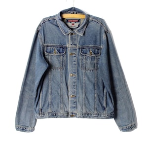 Könnte beinhalten: Eine hellblaue Jeansjacke mit Knopfleiste und zwei Brusttaschen. Die Jacke hat ein Markenetikett mit der Aufschrift "Basic Edition" und einem Flügellogo.