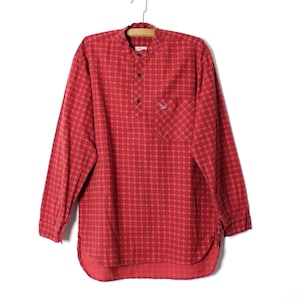 May include: Red plaid long-sleeve shirt with a mandarin collar and a small chest pocket. The shirt is hanging on a hanger against a white background. The shirt has a button-down placket and a rounded hem.