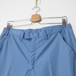 K&ouml;nnte beinhalten: Eine hellblaue Hose, die an einem Holzb&uuml;gel h&auml;ngt. Die Hose hat einen Rei&szlig;verschluss und einen Knopf vorne, zwei Vordertaschen und zwei Ges&auml;&szlig;taschen.
