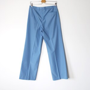 K&ouml;nnte beinhalten: Eine hellblaue, weite Hose, die an einem Holzb&uuml;gel an einer wei&szlig;en Wand h&auml;ngt.