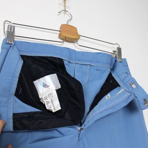 K&ouml;nnte beinhalten: Eine hellblaue Hose mit schwarzem Bund und Rei&szlig;verschluss. Die Hose hat ein Etikett mit der Aufschrift "65% Polyester & 35% Baumwolle" und ein kleines Logo mit einem Vogel.