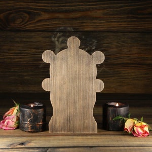 May include: A wooden cutout of a stylised tree with a rustic brown finish. The cutout is placed on a wooden surface with two black candle holders on either side.