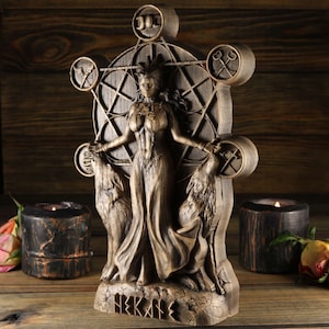 May include: A wooden statue of a goddess with wolves on either side. The goddess is standing in a circle with symbols around her. The statue is painted in a brown and gold colour and has the word "HEKATE" written on the base.