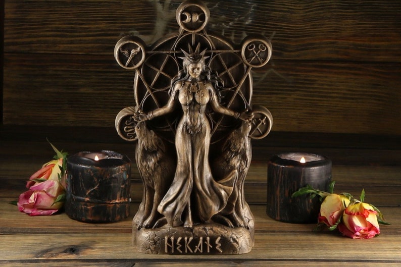 May include: A wooden statue of Hekate, the Greek goddess of witchcraft, magic, and crossroads. She is depicted standing with two wolves on either side of her, and a pentagram behind her. The statue is painted in a dark brown colour and has a rustic finish.