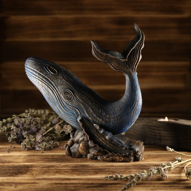 A full side view of the hand-carved wood blue whale figurine, showcasing the detailed ocean decor sculpture facing left. The sea animal sculpture features intricate textures, deep blue tones, and an upward-curved tail.