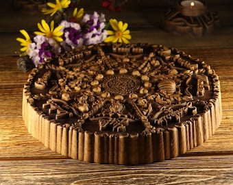 May include: A round wooden wall hanging with intricate carvings of flowers, leaves, and other natural elements. The carving is in a dark brown color and has a raised, textured design.