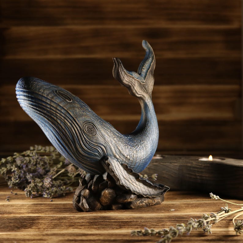 A full side view of the hand-carved wood blue whale figurine, showcasing the detailed ocean decor sculpture facing left. The sea animal sculpture features intricate textures and deep blue tones with an upward-curved tail.