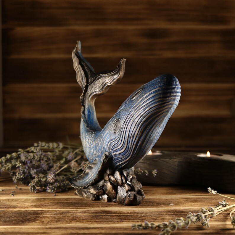 A full side view of the hand-carved wood blue whale figurine, showcasing the detailed ocean decor sculpture with an arched tail. The sea animal sculpture features intricate textures and deep blue tones.