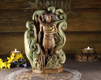 May include: A detailed statue of a figure holding a boat, surrounded by swirling green accents. The figure is in a bronze color, with a spear in one hand. Two lit candles and flowers are in the background. The statue is on a decorative surface.