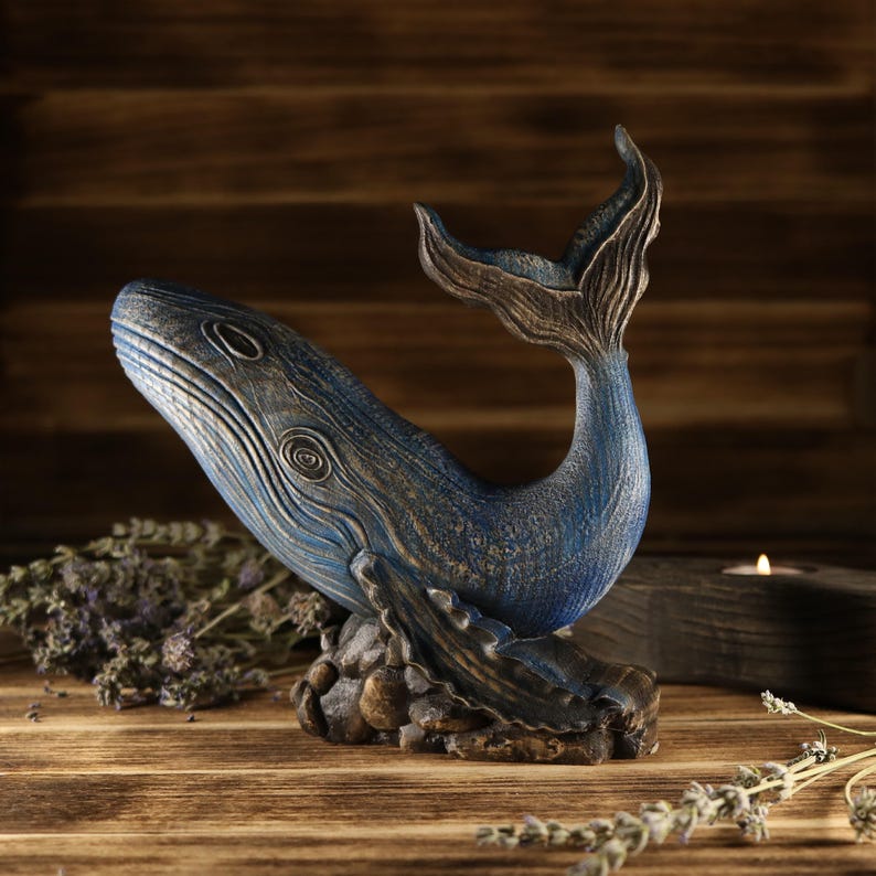 A full side view of the hand-carved wood blue whale figurine, showcasing the detailed ocean decor sculpture facing left. The sea animal sculpture features intricate textures, deep blue tones, and an upward-curved tail.