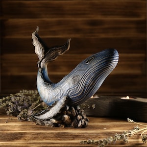 A full side view of the hand-carved wood blue whale figurine, showcasing the detailed ocean decor sculpture with an arched tail. The sea animal sculpture features intricate textures and deep blue tones.