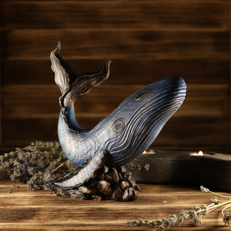 A full side view of the hand-carved wood blue whale figurine, showcasing the detailed ocean decor sculpture with an arched tail. The sea animal sculpture features intricate textures and deep blue tones.