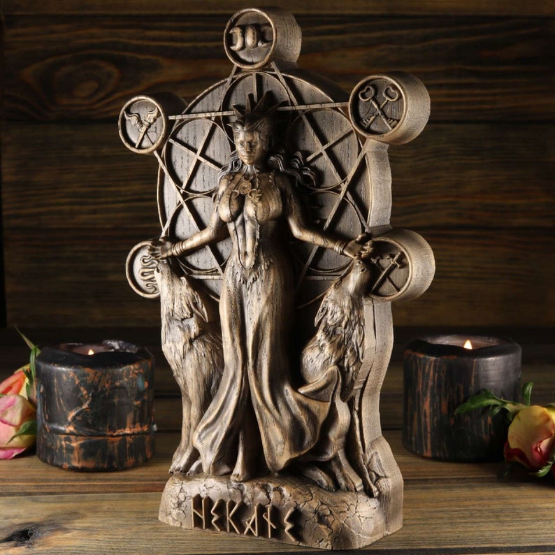 May include: A wooden statue of a goddess with wolves on either side. The goddess is standing in a circle with symbols around her. The statue is painted in a brown and gold colour and has the word "HEKATE" written on the base.