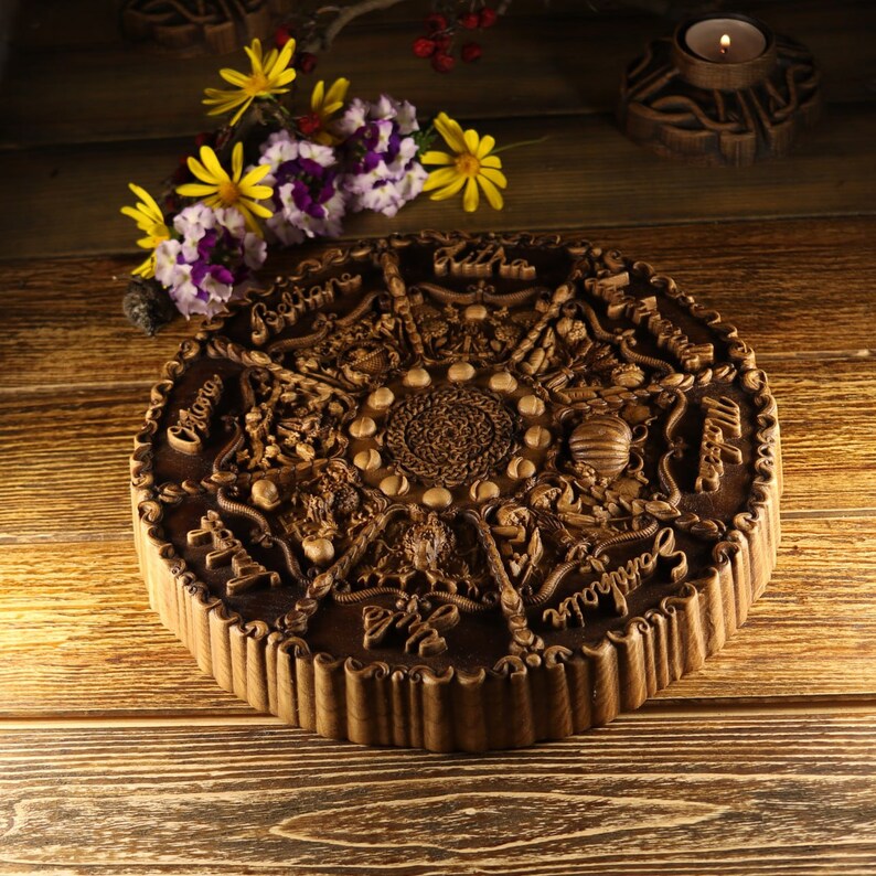 Peut inclure: Une d&eacute;coration murale ronde en bois avec des sculptures complexes repr&eacute;sentant une roue de calendrier. La roue comporte douze sections, chacune avec un symbole et une inscription diff&eacute;rents. Le centre de la roue a un motif circulaire avec un motif de corde tress&eacute;e.