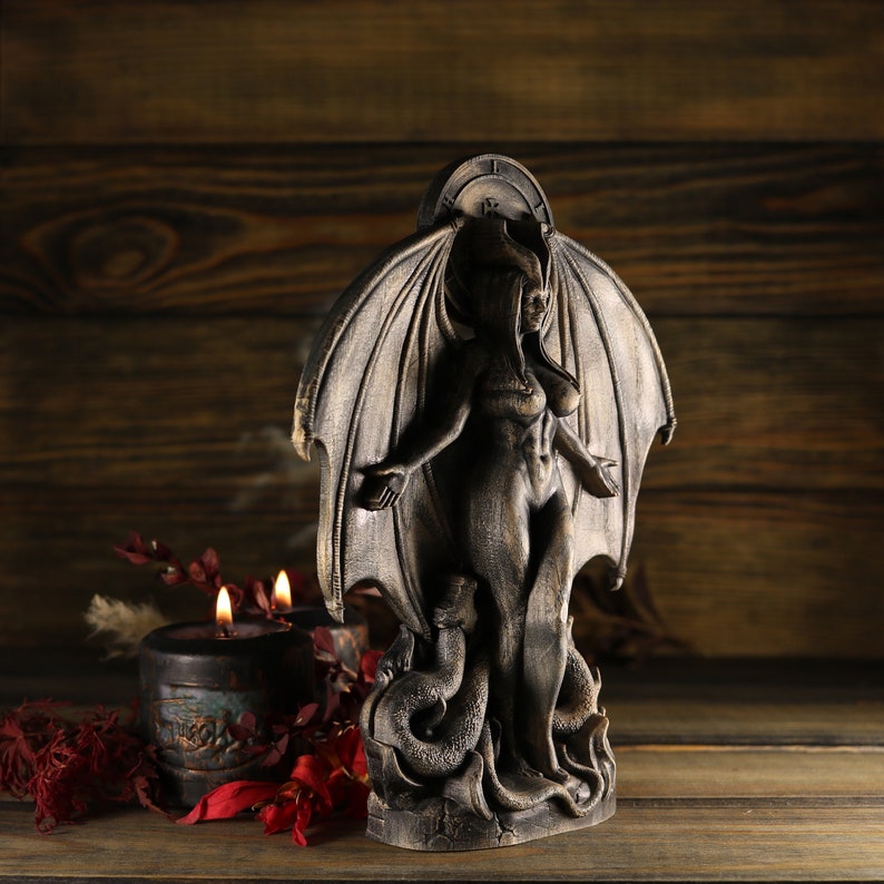 May include: A dark wooden statue of a winged female figure with a clock face above her head. The figure is standing on a serpent and has a dark, weathered finish.