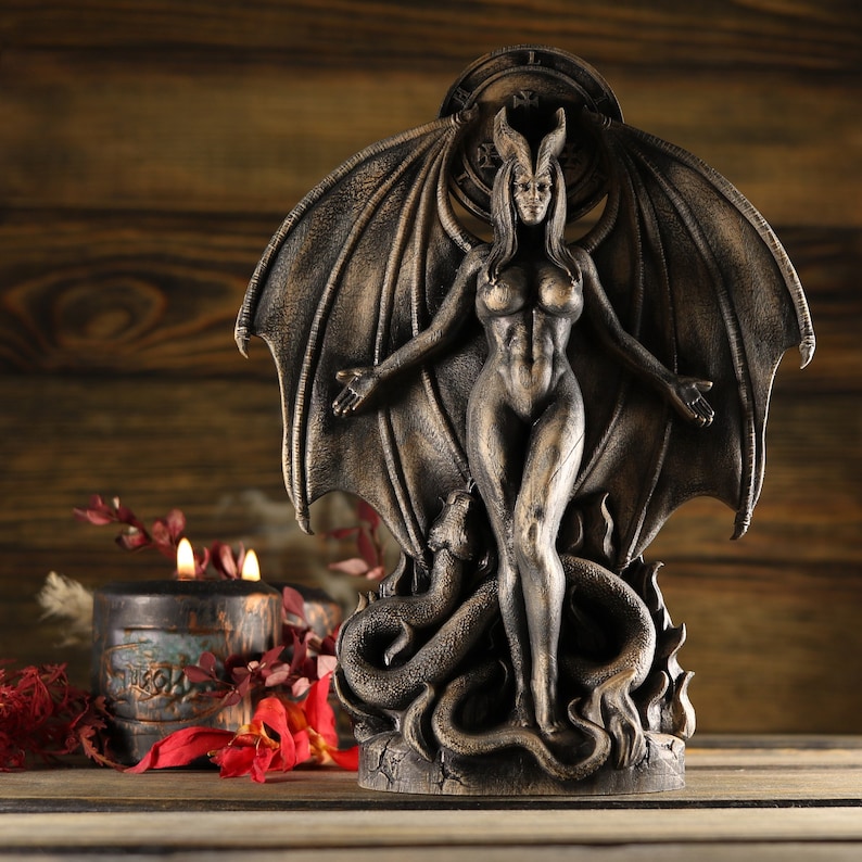 May include: A bronze statue of a female figure with wings and a serpent, standing on a base with a circular design. The figure has a fierce expression and is holding her arms out to the sides.
