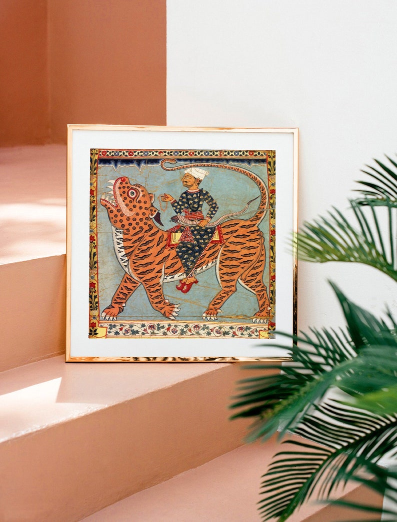 Puede incluir: Una ilustraci&oacute;n enmarcada de una persona montando un tigre. El tigre es naranja y negro con un fondo azul. La persona lleva un atuendo azul y blanco y un turbante. El marco es dorado.