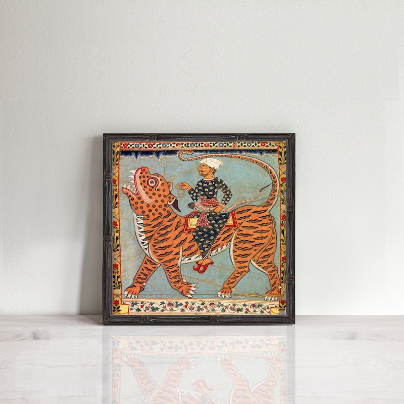 Puede incluir: Una ilustraci&oacute;n enmarcada de un hombre montando un tigre. El hombre lleva un turbante y una t&uacute;nica azul y dorada. El tigre es naranja y negro sobre un fondo azul. El marco es de color marr&oacute;n oscuro con un dise&ntilde;o floral.