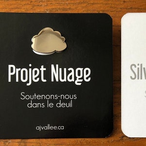 Peut inclure: Deux cartes avec une épingle en forme de nuage argenté sur chacune. La carte de gauche est noire avec du texte blanc qui dit "Projet Nuage" et "Soutenons-nous dans le deuil" et "ajvallee.ca". La carte de droite est blanche avec du texte gris qui dit "Silver Cloud Project", "Supporting each other in mourning", et "ajvallee.ca".