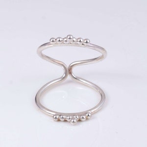 Könnte beinhalten: Ein silberner Ring mit einem doppelten Band und einer Reihe kleiner Perlen auf jeder Seite.